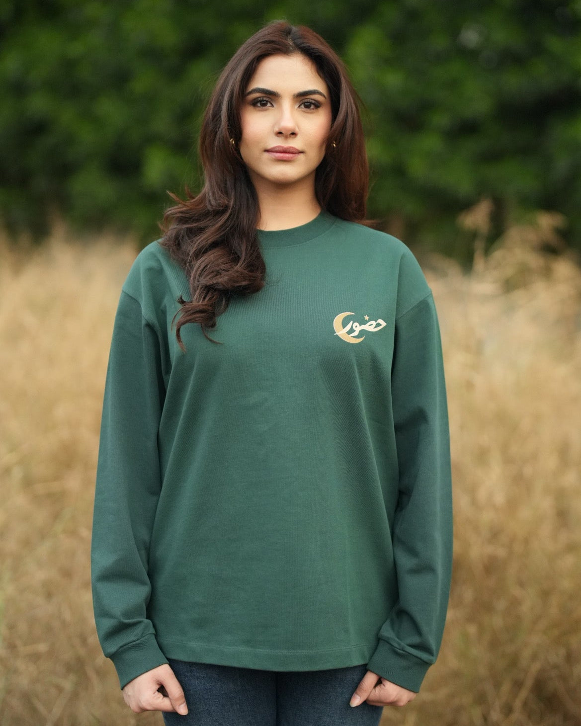 Woman wearing a green long-sleeve shirt with a logo in a field